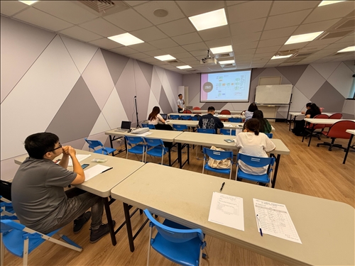 從後方觀察整體教室場景，學生們正聆聽講師說明商品分類與排放模組，教室秩序良好，互動氛圍積極。