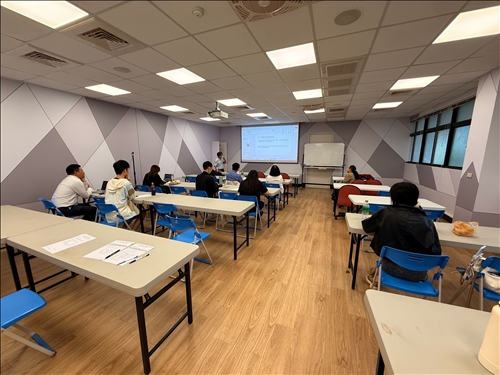 全班專注聆聽老師講解手冊內容，畫面可見簡報畫面逐頁投影，清晰條列CBAM的報告章節與格式規範。