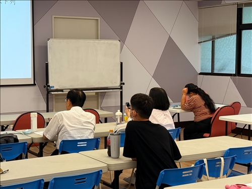 從學員的角度捕捉課堂氛圍，畫面右方的學生正積極記錄筆記並與投影片內容對照。